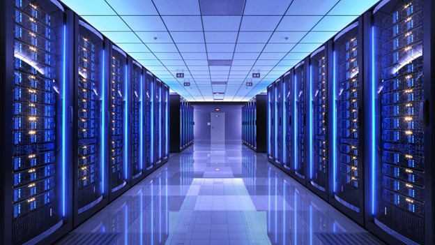 Interior of a modern data centre with rows of illuminated server racks on both sides, glowing blue lights and a reflective tiled floor under a grid-patterned ceiling.